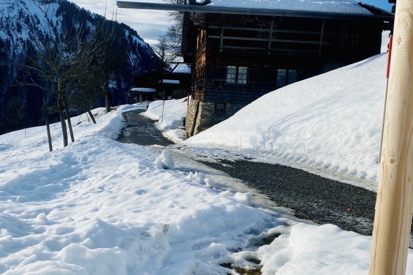 Verschneite Almhütte mit dunklem Holz und schneebedecktem Dach an einem Wanderweg im Allgäu