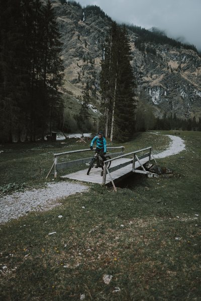Mountainbiker auf einer Holzbrücke im Oytal bei Oberstdorf, dahinter die Felswände