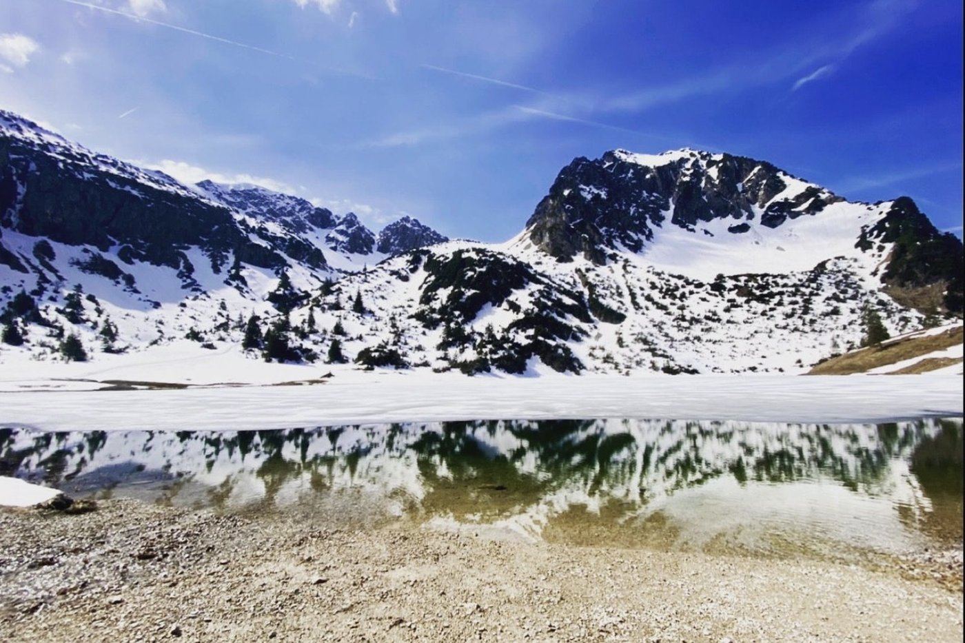Gaisalpsee in spring with a half-frozen surface, mountains reflected in the open water