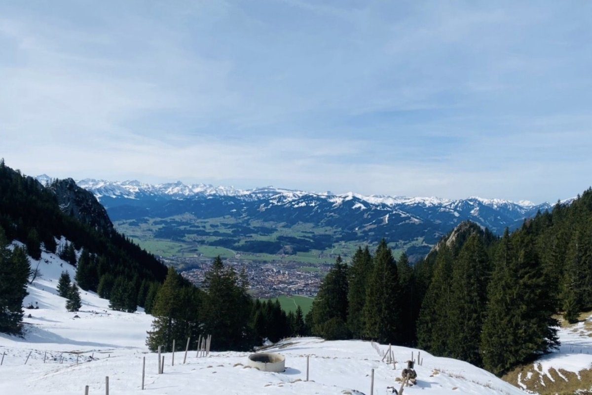 View from the ridge down to Oberstdorf in the valley, late winter with partly snow-covered meadows, Allgäu Alps on the horizon
