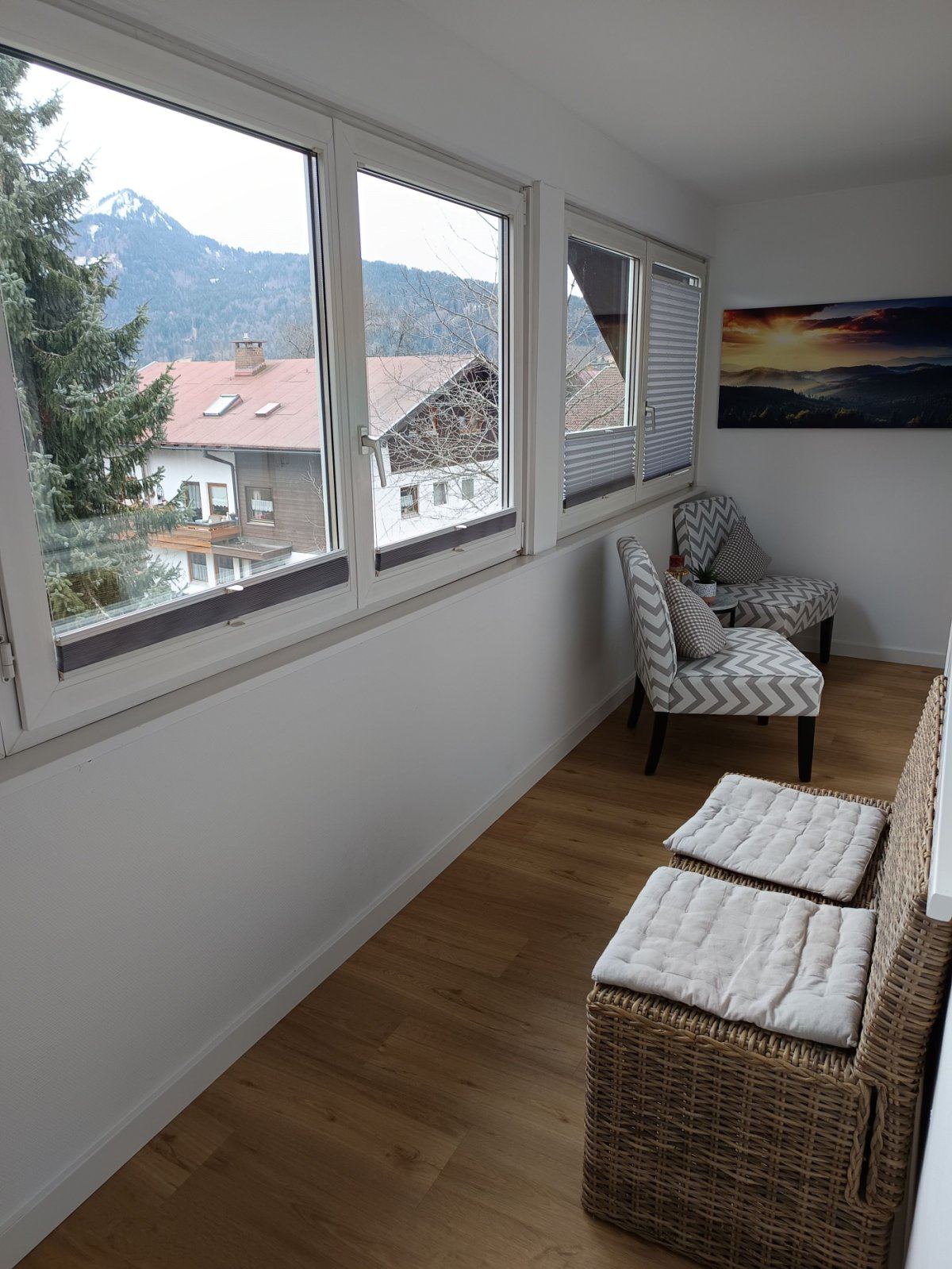 Verglaster Sun Room mit Korbsesseln, Blick über die Dächer auf den verschneiten Berg.