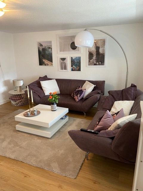 Wohnzimmer mit zwei dunkelvioletten Ledersofas, Bogenlampe, Galerie-Wand mit Bildern, weißer Couchtisch mit Kerzen.