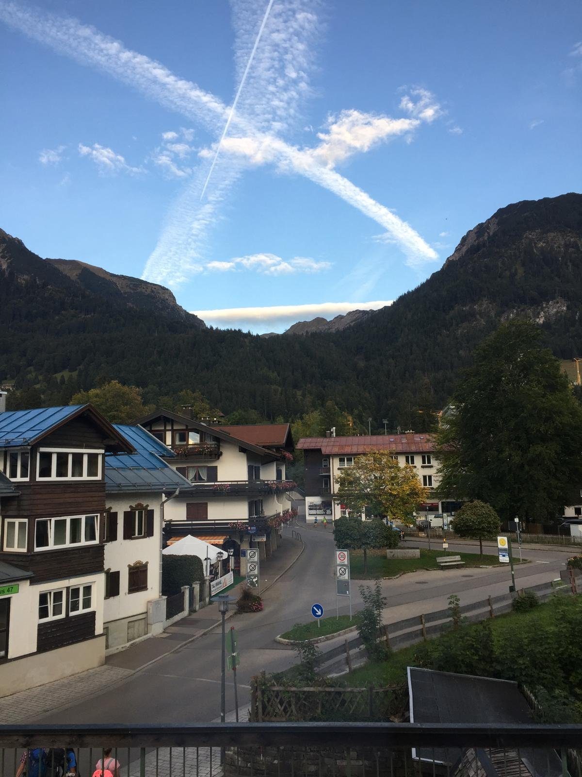Sommerabend mit X-förmigen Kondensstreifen über den Bergen, Blick aus dem Hannes-Fenster über die Häuser von Oberstdorf
