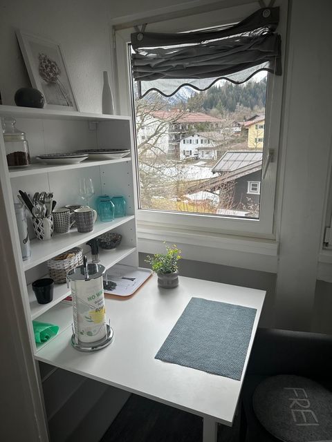 Klapptisch in der Küchenzeile mit Bergblick aus dem Fenster — Allgäuer Holzhäuser im Vordergrund, verschneite Berge im Hintergrund.