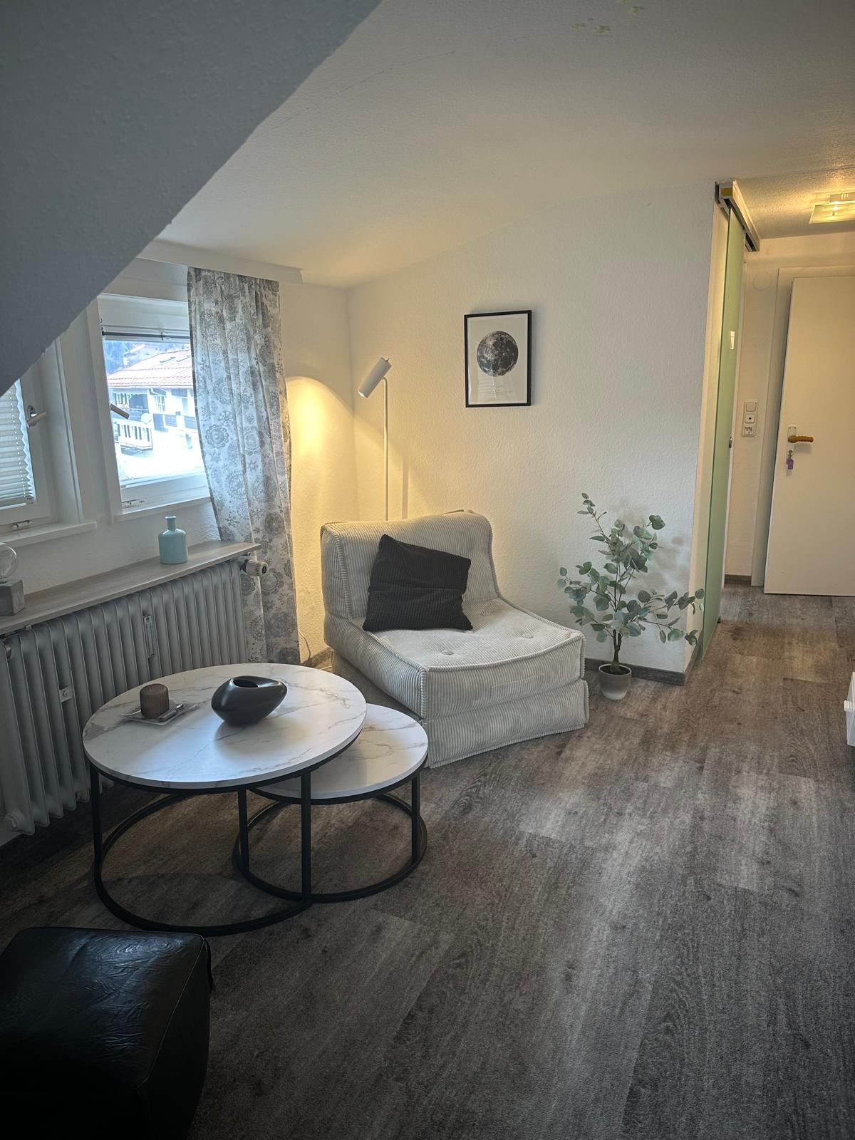 Wohnbereich des Appartements Hannes mit hellem Sessel am Fenster, runden Marmortischen und Stehlampe.